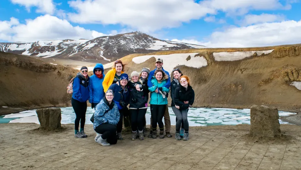 A group of students in winter gear stand in front of a crater filled with frozen glacier water